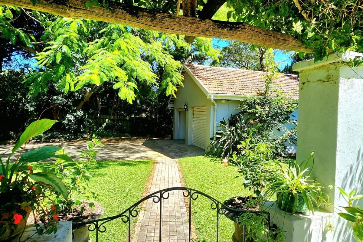 A view of the rear garden featuring a paved walkway leading to a detached garage, framed by a pergola and mature greenery.