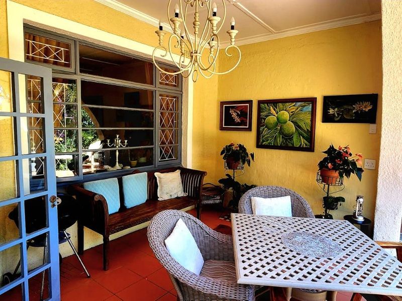 A covered outdoor patio area featuring tiled flooring, wrought iron window frames, and a decorative chandelier, providing a comfortable space for outdoor relaxation.