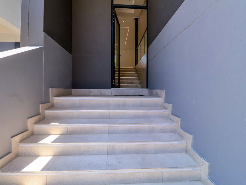 A modern entrance featuring tiled steps leading up to a glass-paneled front door with integrated stair lighting.
