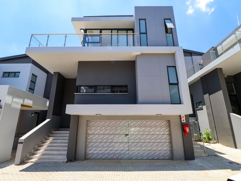 Modern multi-story cluster home featuring a double garage with protective film, glass balcony railings, and contemporary architectural design.