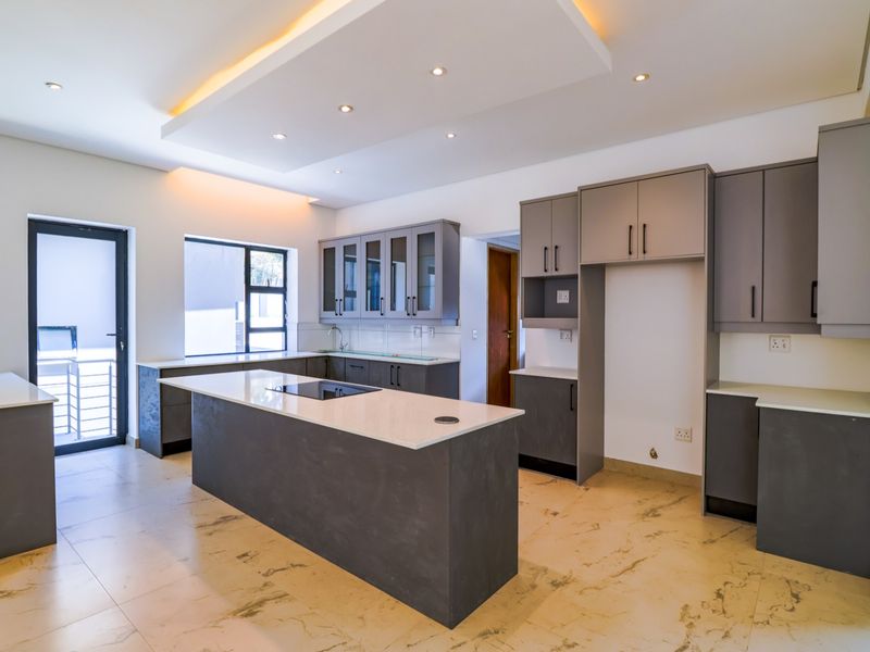 Modern open-plan kitchen featuring a central island with integrated hob, sleek grey cabinetry, stone countertops, and recessed ceiling lighting.