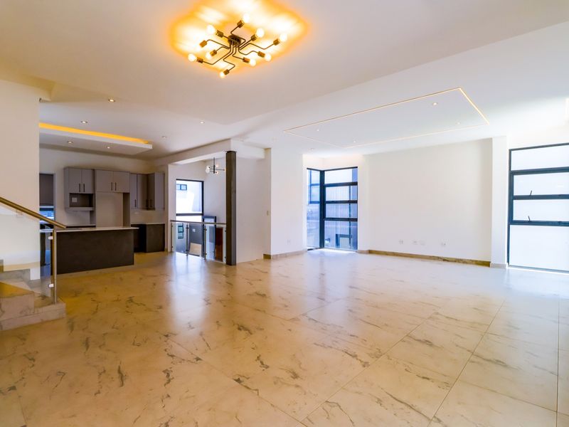 Spacious open-plan living area featuring modern marble-look tiled flooring, recessed ceiling lighting, and a sleek kitchen with built-in cabinetry.
