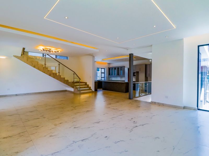 Spacious open-plan living area featuring modern marble-look tiled flooring, a striking staircase with glass balustrades, recessed ceiling lighting, and an integrated kitchen.