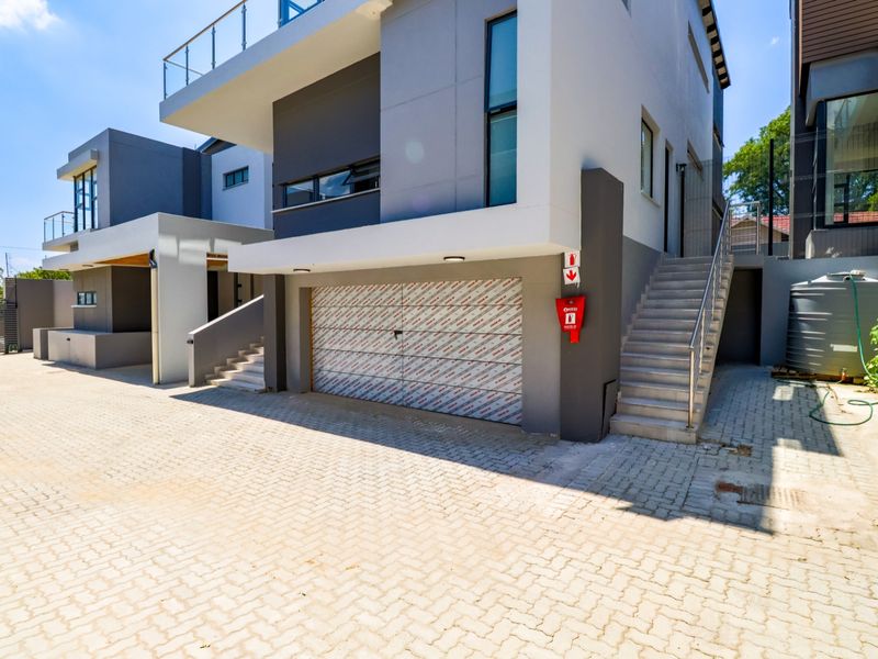 Modern cluster home exterior featuring a double garage with protective film, external staircase, paved driveway, and a water storage tank.