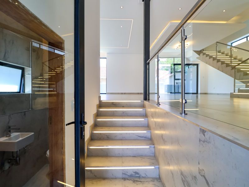 Modern entrance hall featuring marble-tiled stairs with integrated LED lighting, glass balustrades, and a sleek, open-plan layout leading to the main living area.
