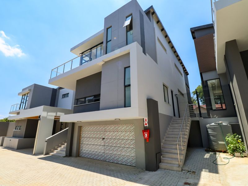 Modern multi-level cluster home featuring a double garage, external staircase, balcony, and contemporary grey and white facade finishes.