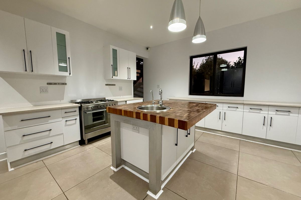 Modern kitchen featuring a central island with a butcher block countertop, stainless steel gas stove, ample white cabinetry, and large format floor tiles.