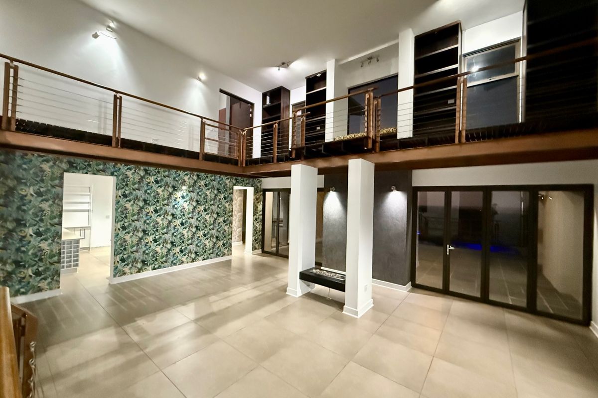 Spacious open-plan living area featuring a mezzanine level, modern tiled flooring, built-in shelving, and large bi-fold doors leading to the exterior.