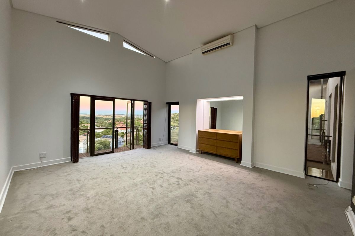 Spacious bedroom featuring high ceilings, recessed lighting, split-system air conditioning, and bi-fold doors opening to a scenic balcony view.