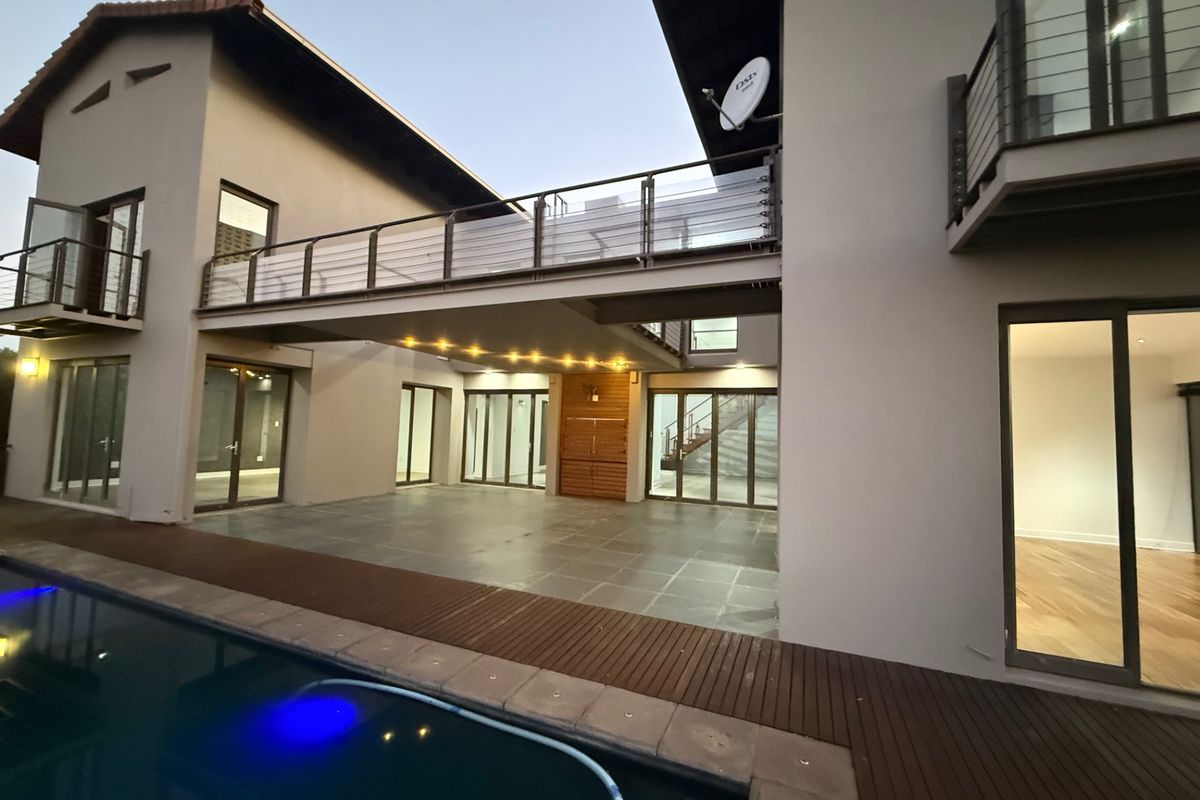 Modern rear exterior featuring a swimming pool, timber decking, stone patio, and an elevated walkway connecting two sections of the home.