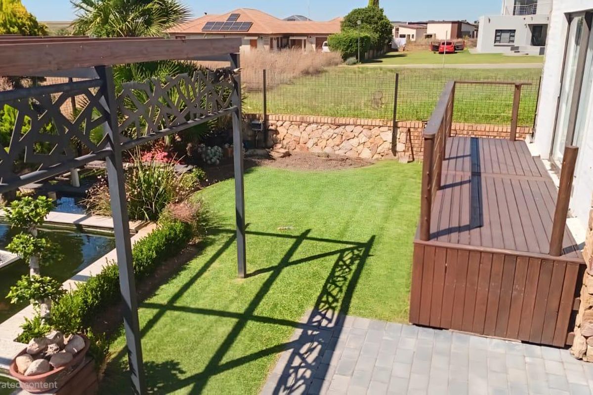 A well-maintained rear garden featuring a raised timber deck, a decorative metal pergola, a koi pond, and stone-clad exterior wall finishes.