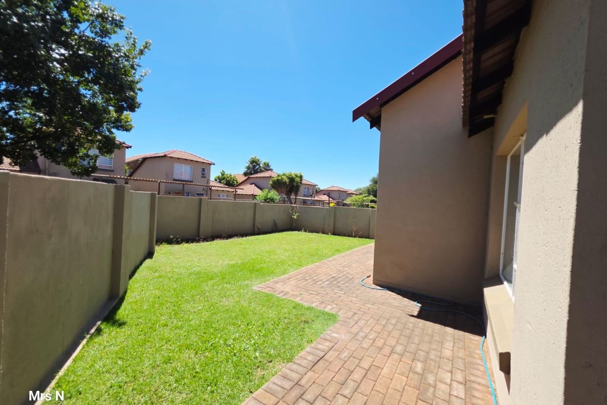 A private rear garden featuring a paved patio area, a well-maintained lawn, and high perimeter boundary walls for added privacy.