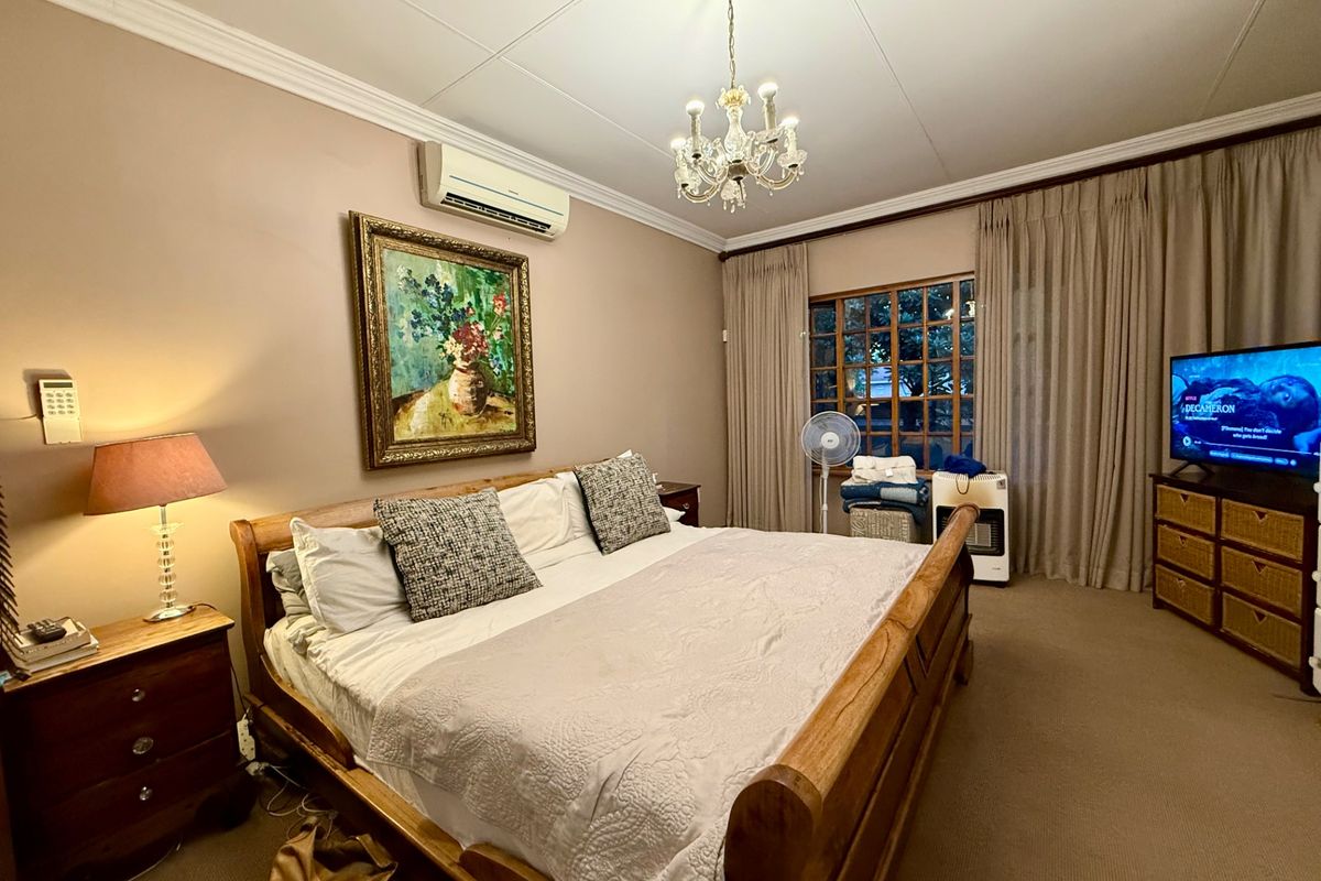 A well-maintained bedroom featuring a split-system air conditioning unit, crown molding, and a large window with curtains.