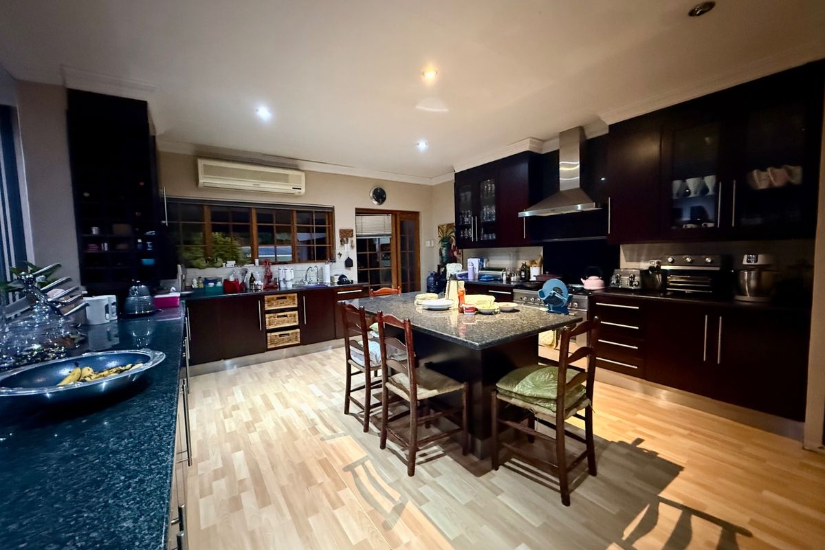 Spacious kitchen featuring dark cabinetry, granite countertops, a central island with seating, and integrated stainless steel extractor fan.