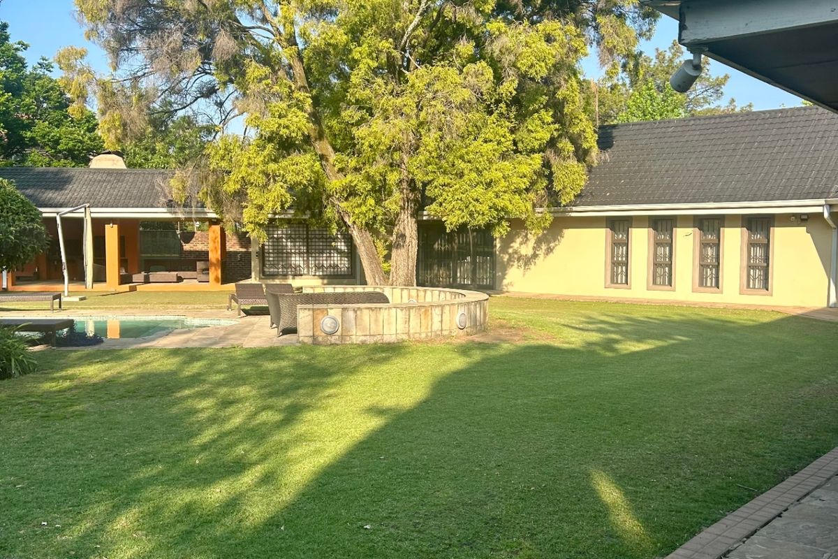 Spacious rear garden featuring a well-maintained lawn, mature tree, paved patio area, and a swimming pool with a stone-walled surround.