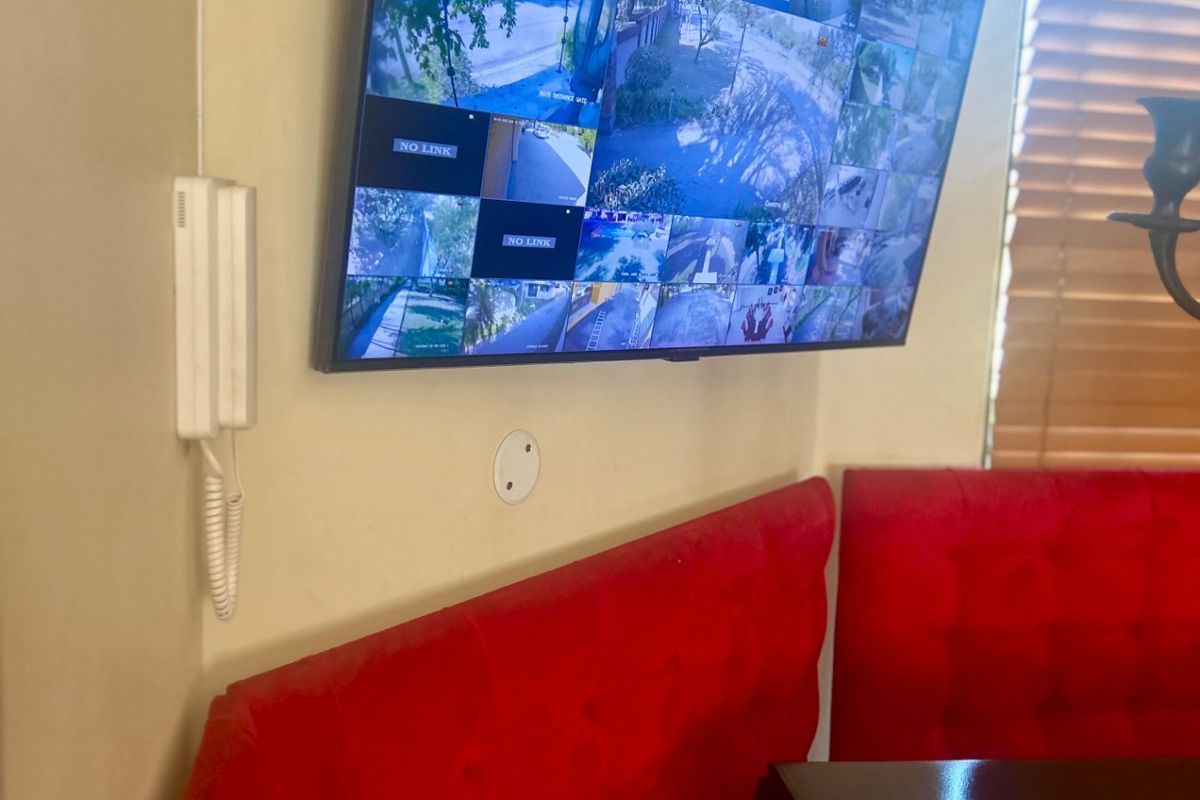 A wall-mounted security camera monitor system integrated into the living space, featuring a wall-mounted intercom unit and wooden window blinds.