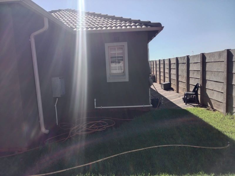 A view of the rear exterior of the house featuring a tiled roof, paved walkway, and a precast concrete boundary wall.