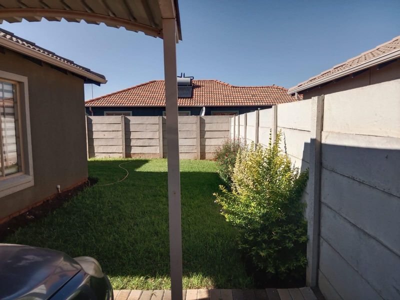 A private rear garden area featuring a lawn, enclosed by precast concrete boundary walls, viewed from a covered patio space.