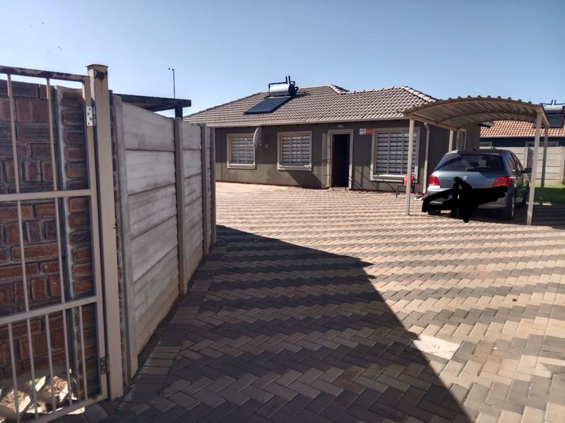 Front exterior view of the house featuring a paved driveway, carport, and solar water heating system installed on the tiled roof.