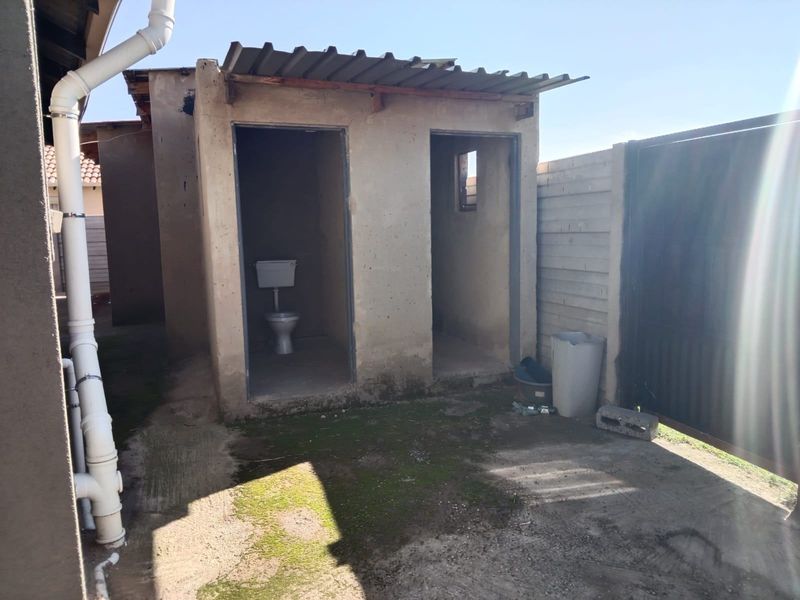 External utility structure featuring two separate compartments, one equipped with a toilet, constructed with basic concrete walls and a corrugated metal roof.