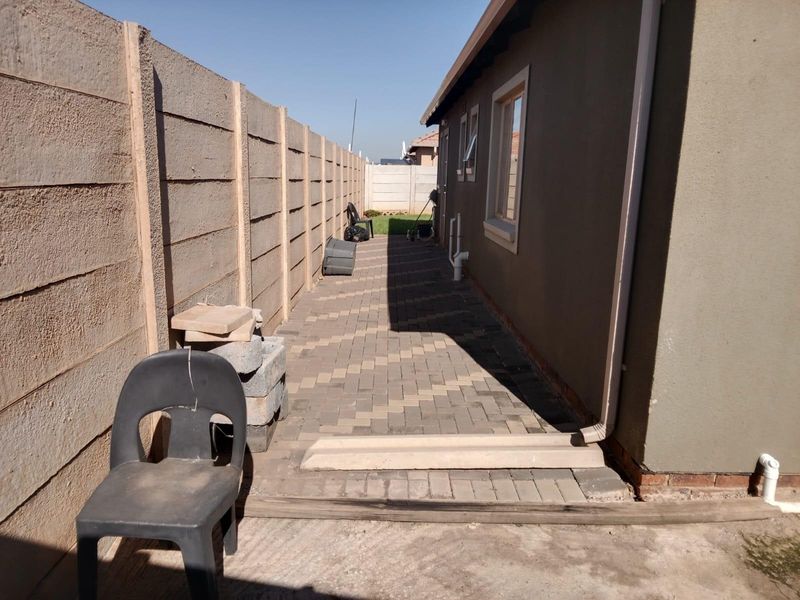 A side exterior view of the property featuring a paved walkway, precast concrete boundary wall, and functional drainage downpipes.