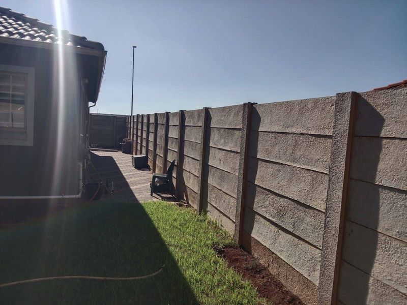 A view of the rear exterior area featuring a paved walkway, a small lawn, and a precast concrete boundary wall.