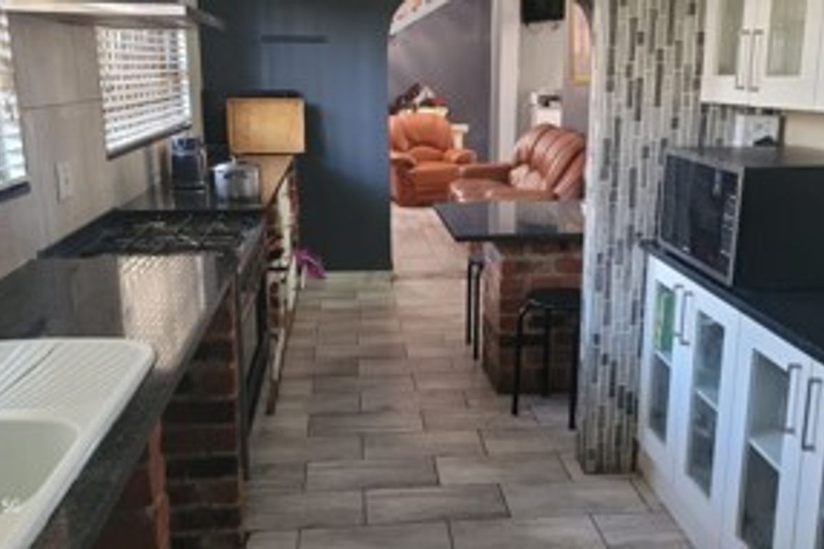 A functional kitchen featuring granite countertops, brick-based cabinetry, and tiled flooring, leading through an archway into the adjacent living area.