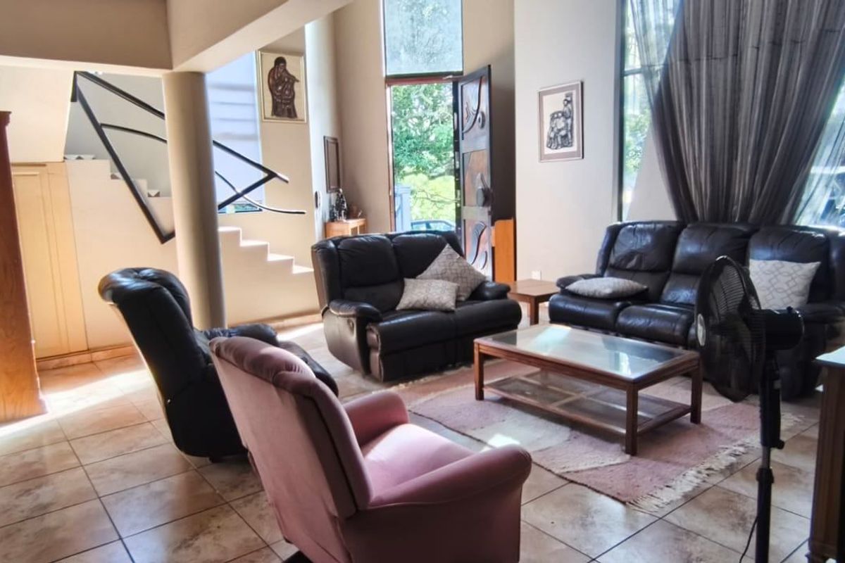 Spacious open-plan living area featuring double volume ceilings, large windows for natural light, and tiled flooring with an integrated staircase.