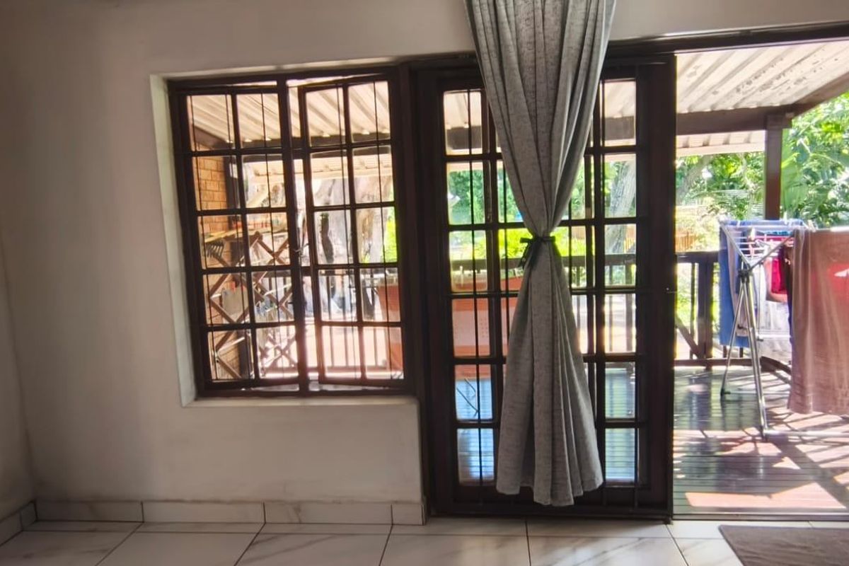 A bright living area featuring tiled floors and timber-framed glass doors leading out to a covered patio space.