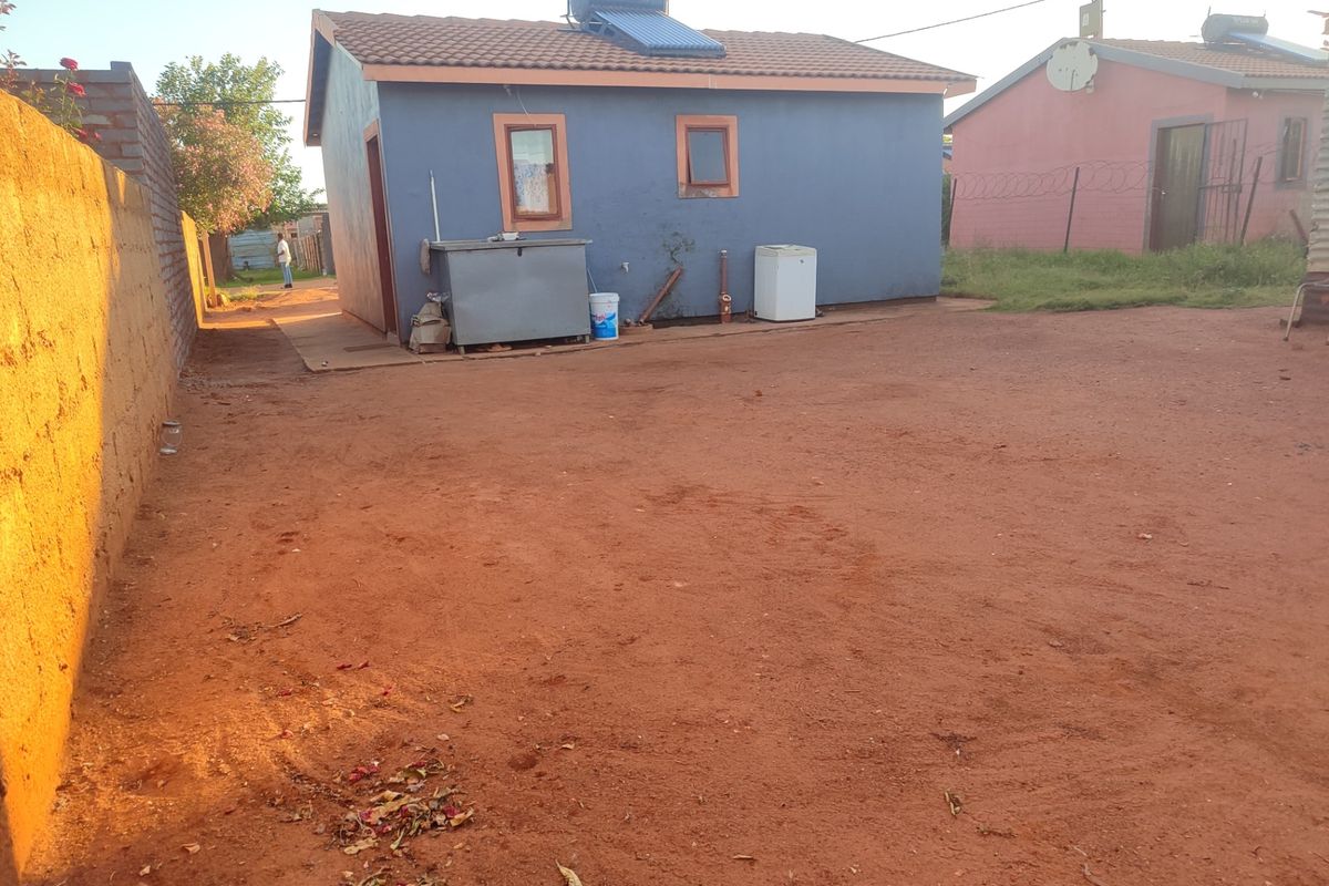 Rear view of a detached house featuring a solar water heating system, tiled roof, and an unpaved yard area.