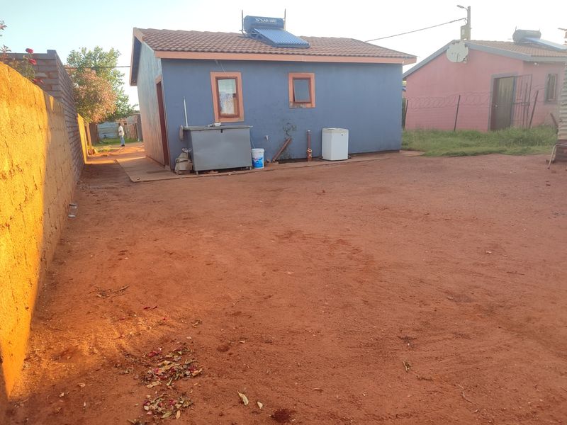 Rear view of a detached house featuring a solar water heating system, tiled roof, and an unpaved yard area.