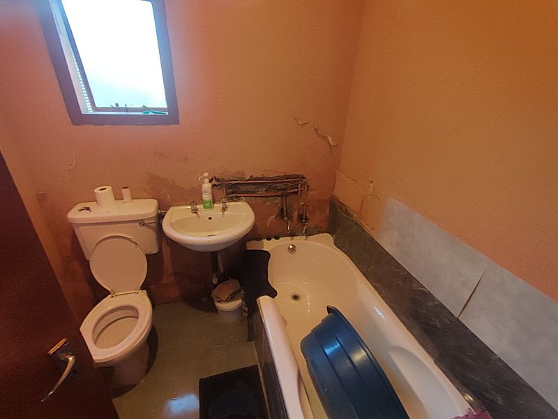 A bathroom in need of significant renovation, featuring a bathtub, pedestal basin, and toilet with visible wall damage and exposed plumbing.