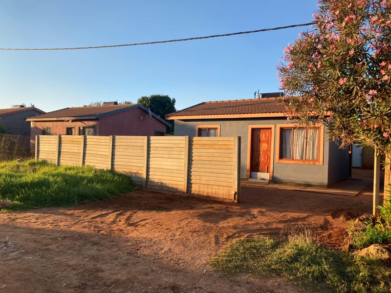 Front view of a single-story residential house featuring a tiled roof, timber entrance door, and a precast concrete boundary wall.