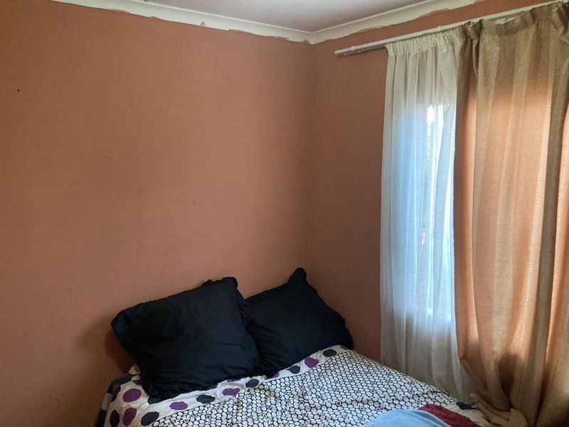 A bedroom featuring a window with a curtain rod and painted walls showing signs of wear near the ceiling cornice.