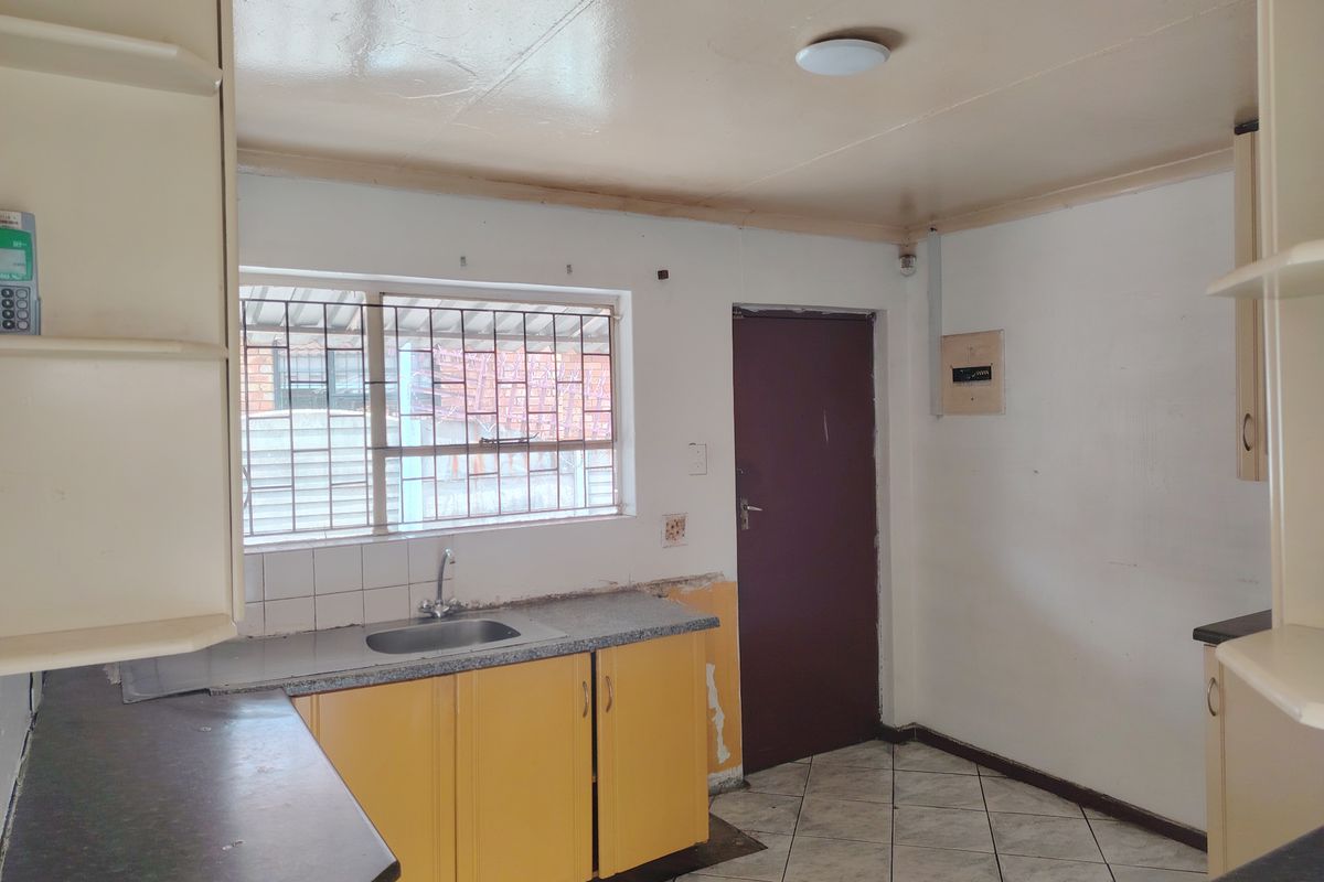 A functional kitchen space featuring built-in cabinetry, a stainless steel sink, and tiled flooring, currently vacant and ready for renovation.