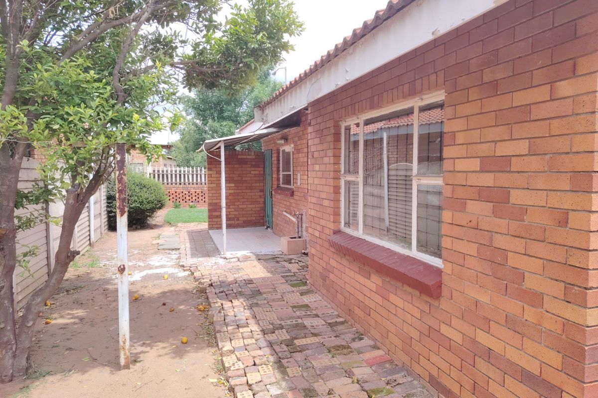 Rear exterior view of a face brick house featuring a paved walkway, covered patio area, and established garden space.