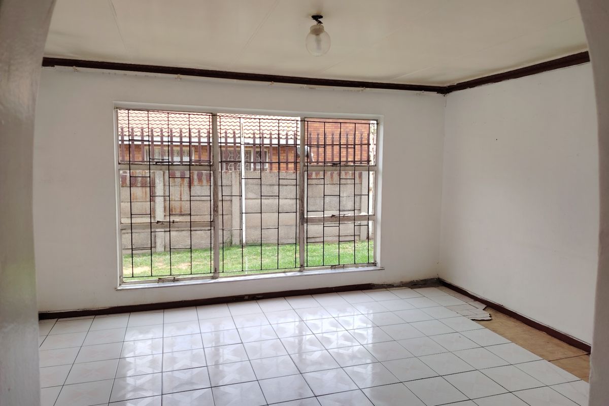 An empty living room featuring white tiled flooring, an arched entrance, and large windows fitted with security bars.