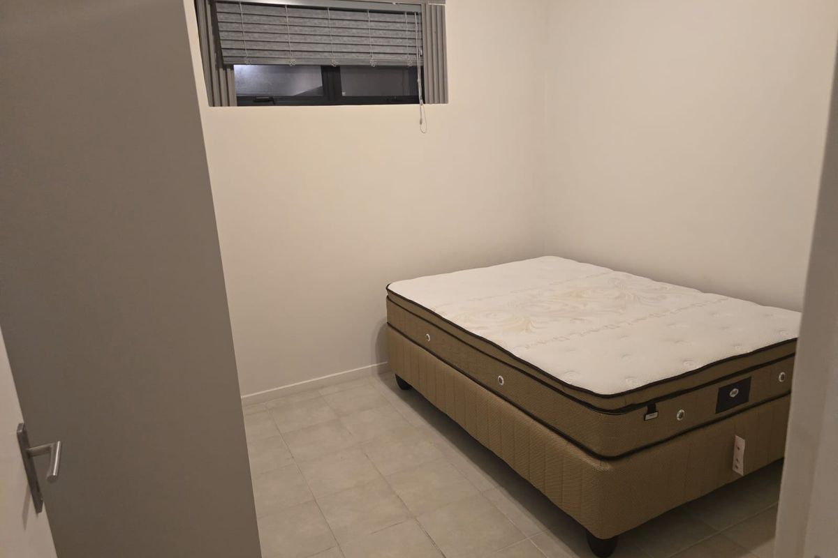 A simple bedroom featuring tiled flooring and a window with fitted horizontal blinds, offering a neutral space ready for personalization.