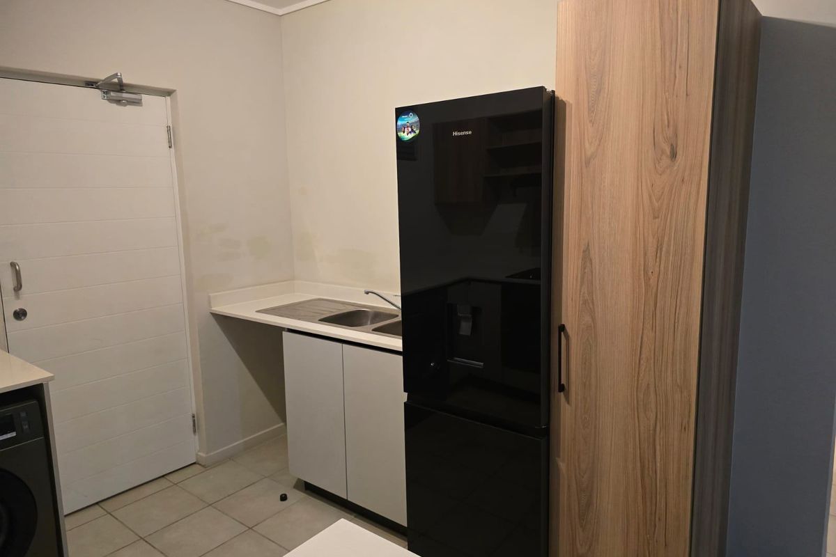 A functional kitchen area featuring built-in cabinetry, a stainless steel sink, and tiled flooring, with neutral wall finishes.