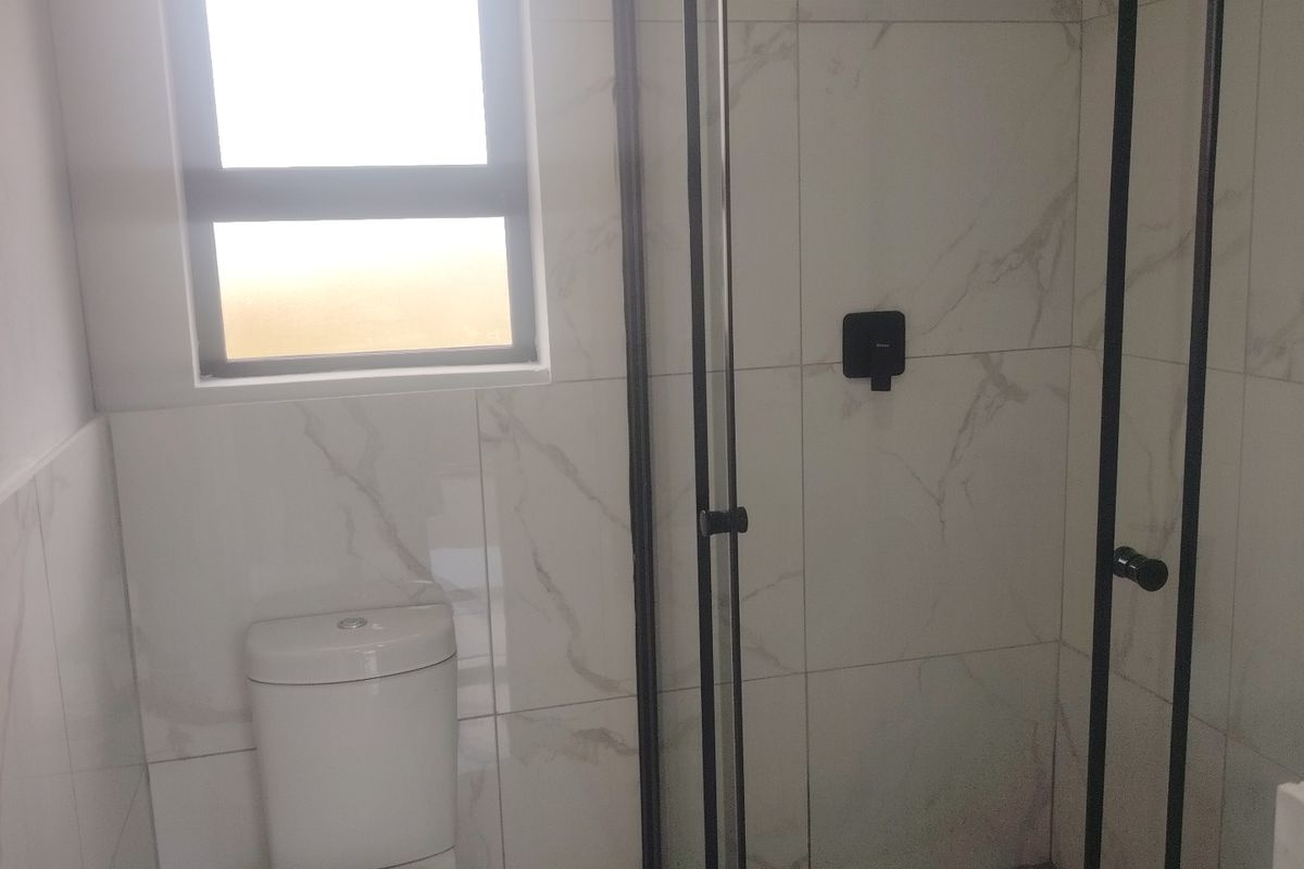 Modern bathroom featuring a walk-in shower with black frame, marble-look wall tiles, hexagonal floor tiles, and a white toilet.