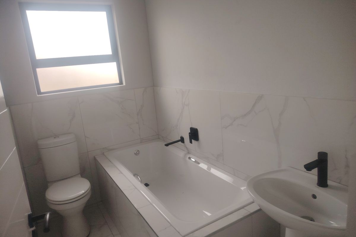 Modern bathroom featuring a built-in bathtub, pedestal basin, and toilet with contemporary matte black fixtures and marble-look wall tiling.