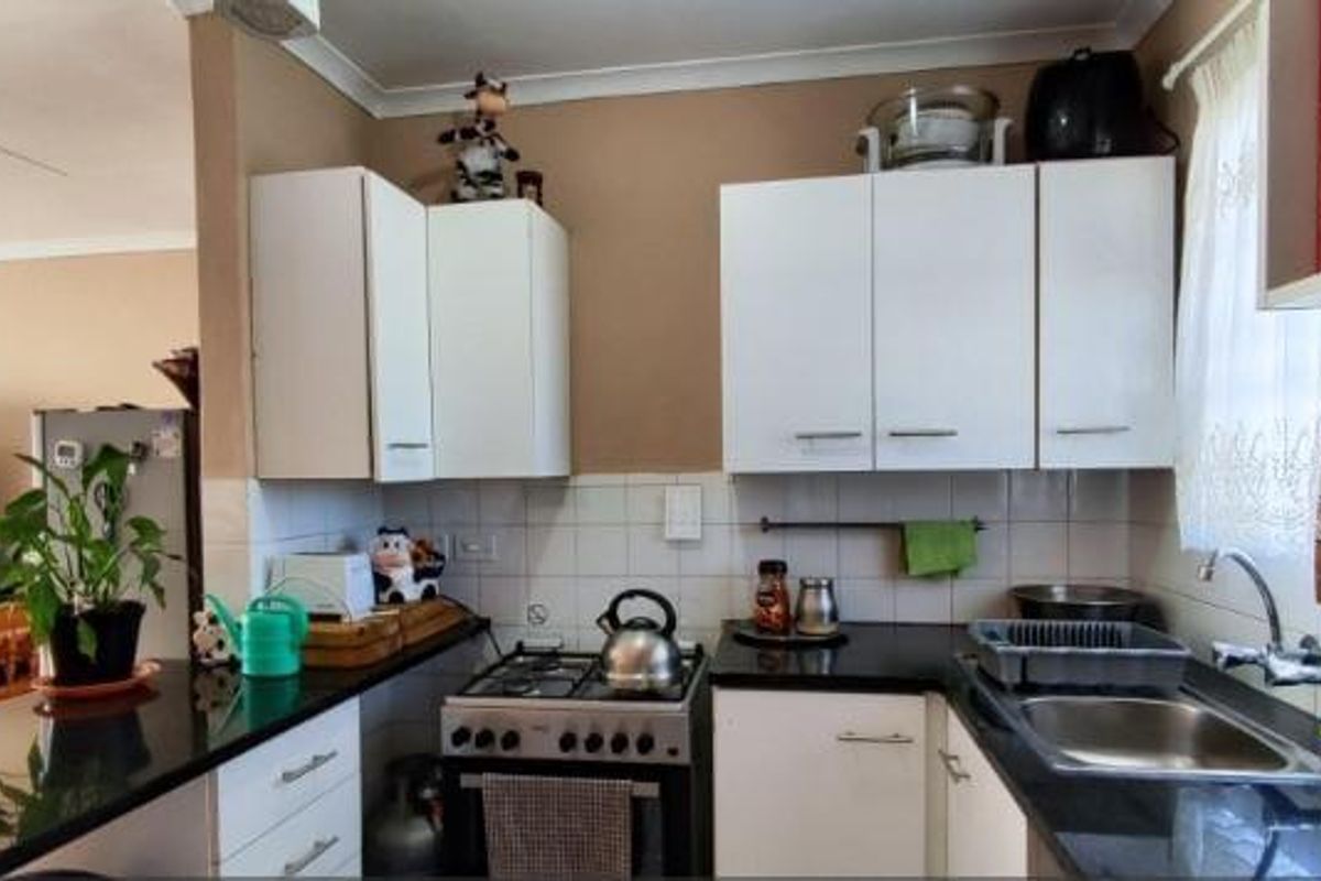 A functional kitchen featuring white cabinetry, granite countertops, a gas stove, and a stainless steel sink with a tiled backsplash.