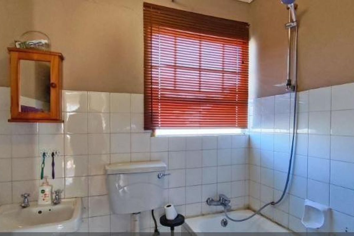 A functional bathroom featuring a pedestal basin, toilet, and bathtub with shower attachment, finished with white wall tiles and wooden venetian blinds.