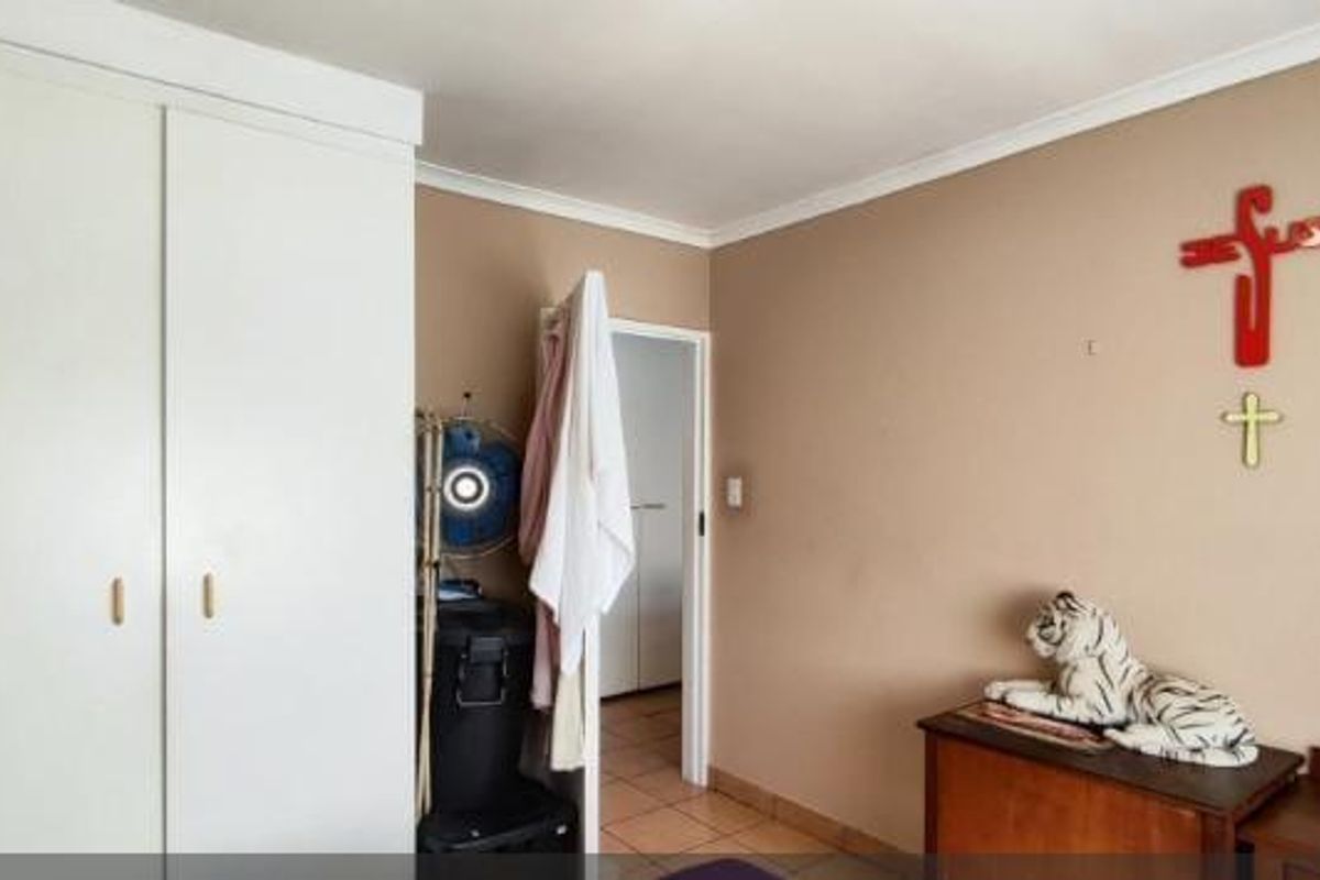 A bedroom featuring built-in cupboards and tiled flooring, offering a functional space with potential for cosmetic updates.
