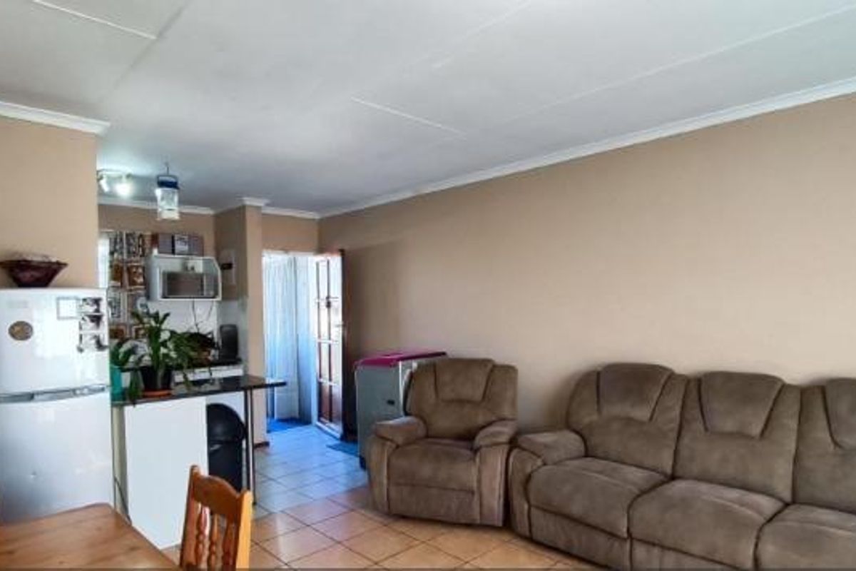 Open-plan living area featuring tiled flooring, a compact kitchen with breakfast counter, and neutral wall finishes, providing a functional and connected living space.