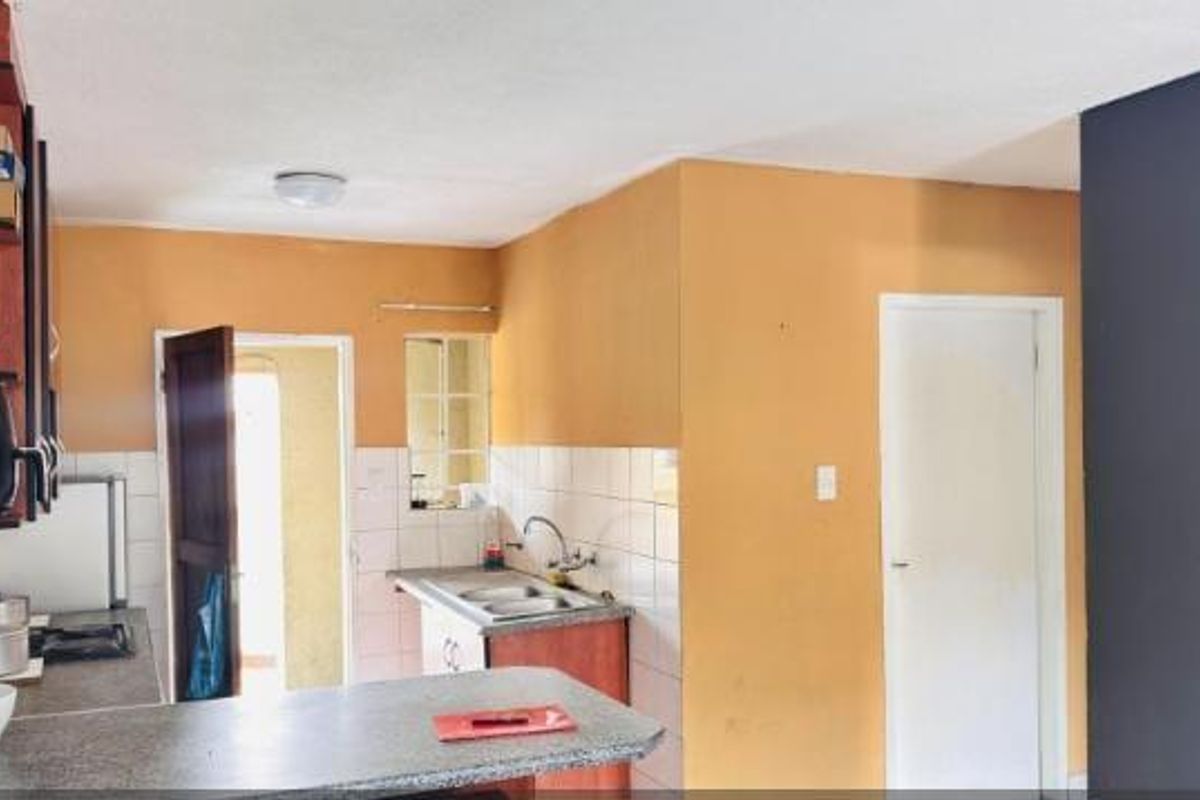 A functional kitchen featuring built-in cabinetry, a double bowl sink, tiled backsplash, and a breakfast bar, offering potential for modernization.