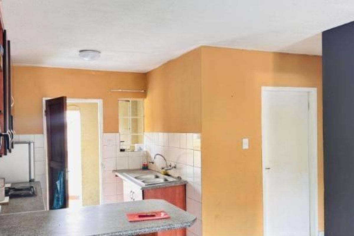 A functional kitchen area featuring built-in cabinetry, a laminate countertop with a stainless steel sink, and tiled backsplash, offering potential for modernization.