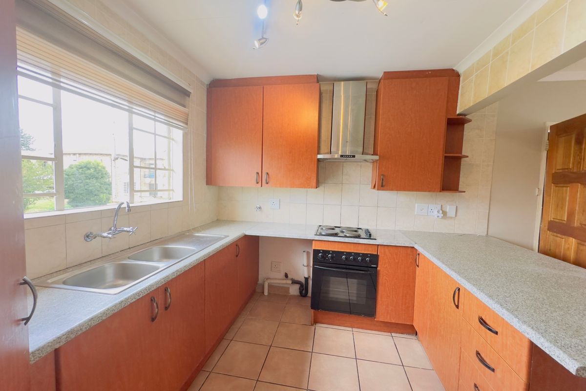 A functional kitchen featuring laminate cabinetry, a double basin sink, built-in oven with gas hob, and tiled finishes throughout.