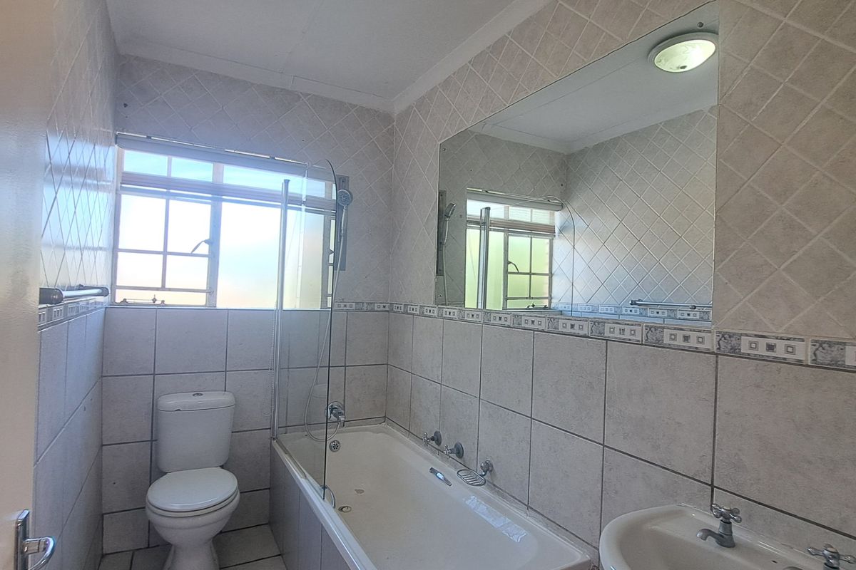 A functional bathroom featuring a bathtub with a glass screen, pedestal basin, toilet, and neutral wall tiling.