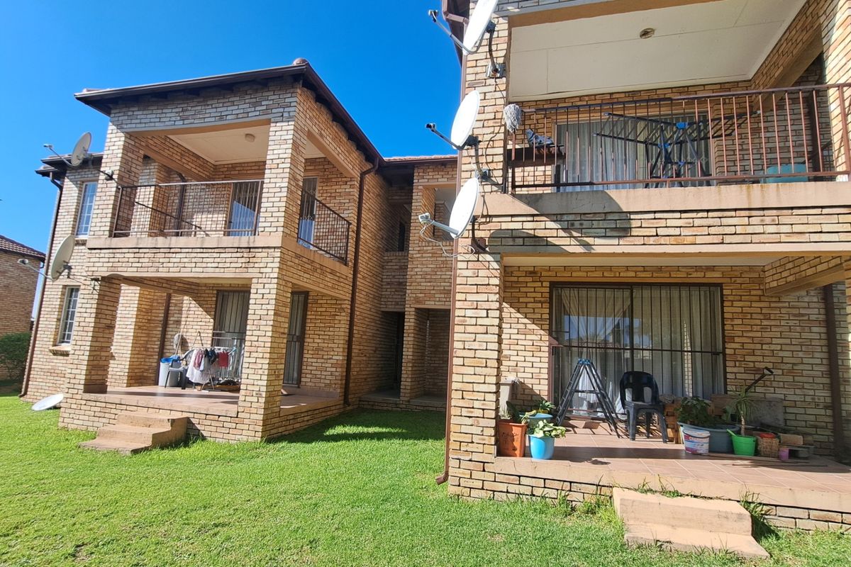 Rear view of a double-story townhouse complex featuring face brick construction, covered balconies, and ground-floor patios overlooking a shared lawn area.